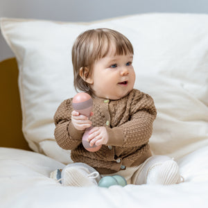 A baby is playing with rattle set mini while sitting on a FLEXA Dots single bed