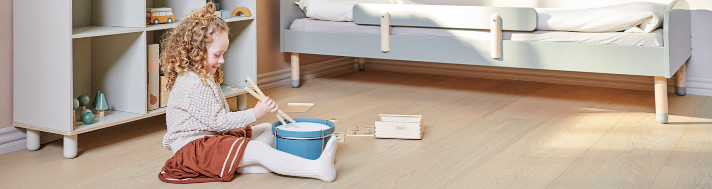 Girl is playing with her FLEXA wooden drum next to her Dots single bed