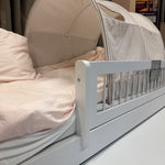 FLEXA white children’s bed with safety rail, striped canopy, pink bedding and books on shelf in a child’s room.