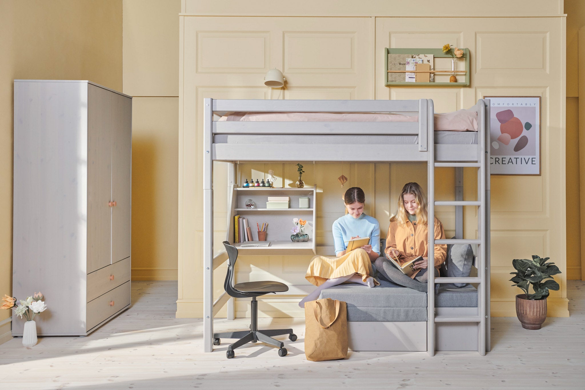 Lit mezzanine FLEXA gris avec canapé, échelle et barrière de sécurité, dans une chambre lumineuse agrémentée détagères, de plantes et de décorations murales.