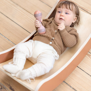 Toddler lying on wooden FLEXA Play Balance Board from FLEXA and playing with Rattle Set