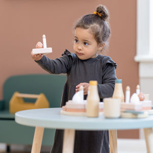 Girl is standing at her Dots play table while playing with the wooden birthday cake from FLEXA