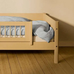 FLEXA SAND short safety rail from WHITE & NOR on toddler bed with blue-striped bedding in a beige children’s room.