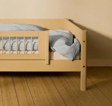 FLEXA SAND short safety rail from WHITE & NOR on toddler bed with blue-striped bedding in a beige children’s room.