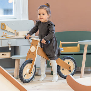 Girl is riding on a FLEXA balance bike in wood