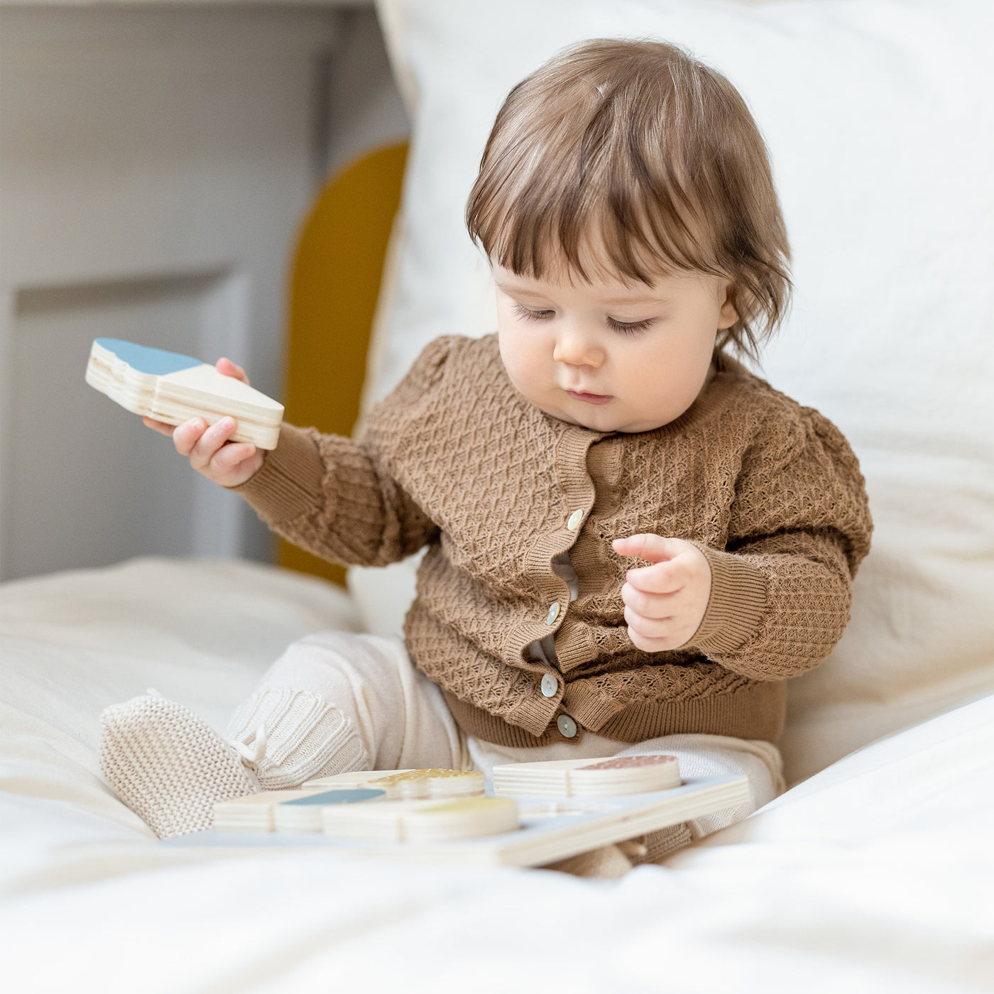 Baby is sitting in a dots single bed while playing with the ice cream puzzle from FLEXA